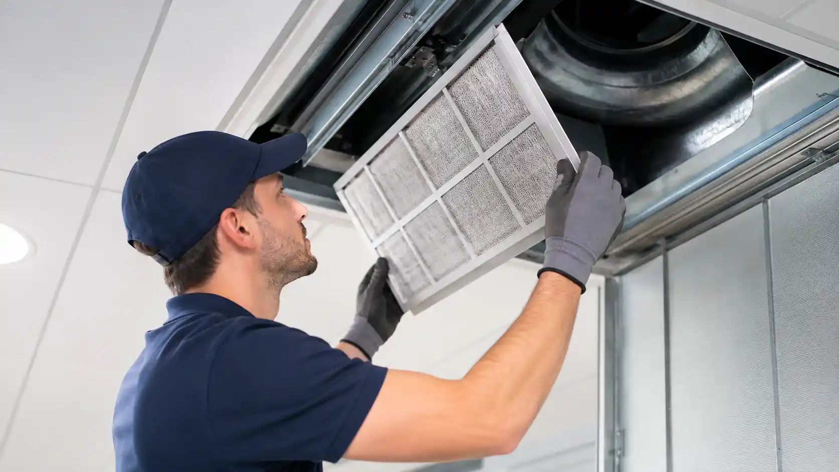 Technician inspecting and cleaning an office HVAC air conditioning unit and filter during summer